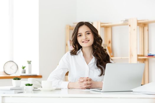 Young businesswoman or secretary sitting at desk and working. Smiling and looking at camera.