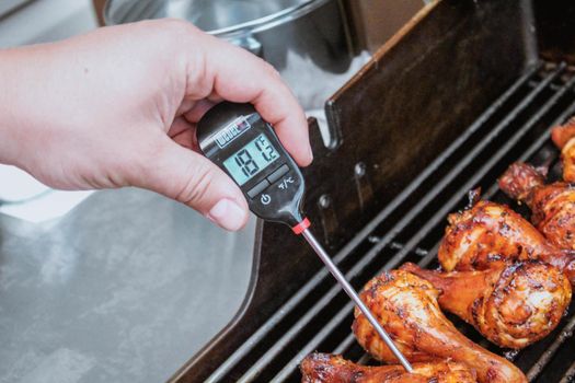 Gatineau, Quebec Canada - July 18, 2020: A food thermometer checking that chicken is being cooked correctly, safely on a barbecue along with prawns on a sunny day in the garden. Weber thermometer