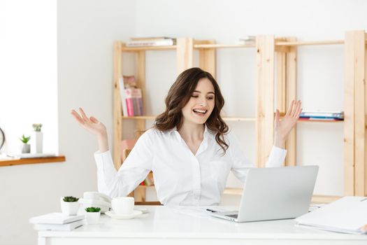 Successful business woman with arms up sitting in modern office