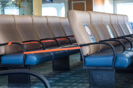 Perspective view of empty seats in the airport with social distancing regulation sign for COVID-19 epidemic awareness. Selective focus.