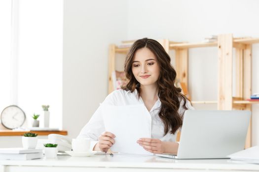 Young businesswoman or secretary sitting at desk and working. Smiling and looking at camera.