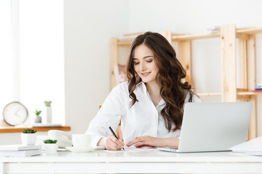 Portrait of a charming businesswoman sitting at her workplace and writing.