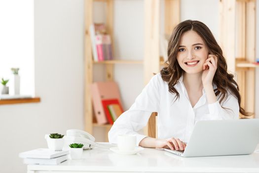 Young businesswoman or secretary sitting at desk and working. Smiling and looking at camera.