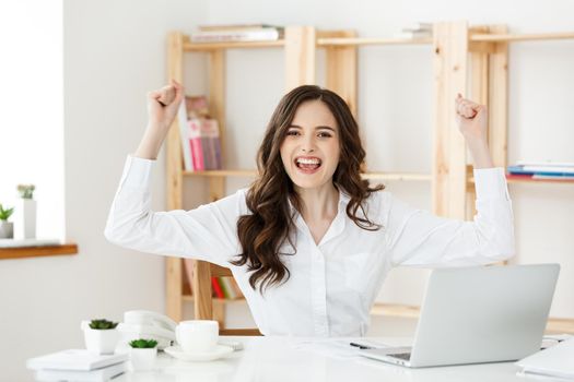 Successful business woman with arms up sitting in modern office