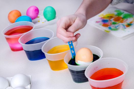 Kid hand paints eggs for easter holidays. Dyeing easter eggs at home. Child creates festive decorations.