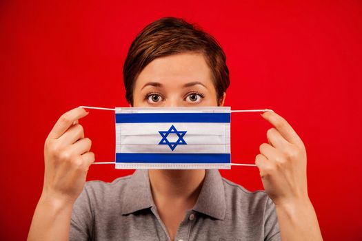 Coronavirus COVID-19 in Israel. Woman in medical protective mask with the image of the flag of Israel. The concept of preventing the spread of the epidemic and treating coronavirus.