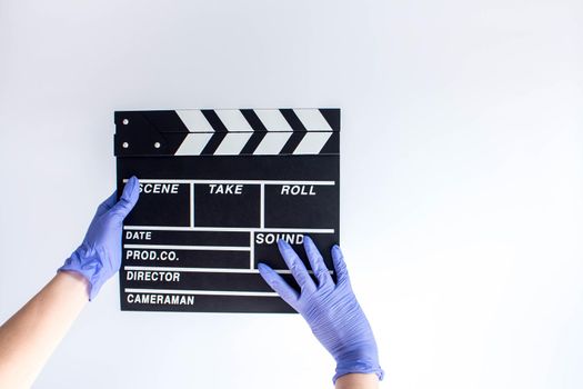 Woman in blue disposable rubber gloves holding movie clapper. Influence of pandemic on cinematography