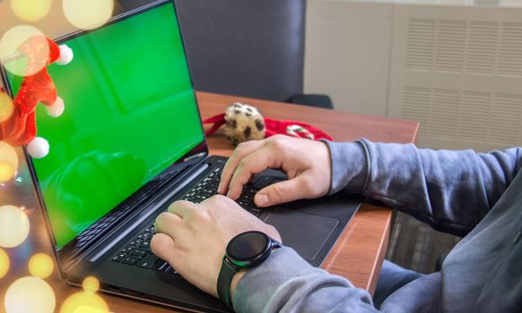 Closeup man hands typing on laptop keyboard with empty green screen and Christmas decoration on background. Holiday concept. Office. Mock-up.