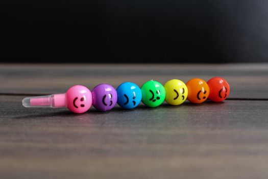 Rainbow pencil with smiles on wooden background. Rainbow pen with smiley faces on wooden background.