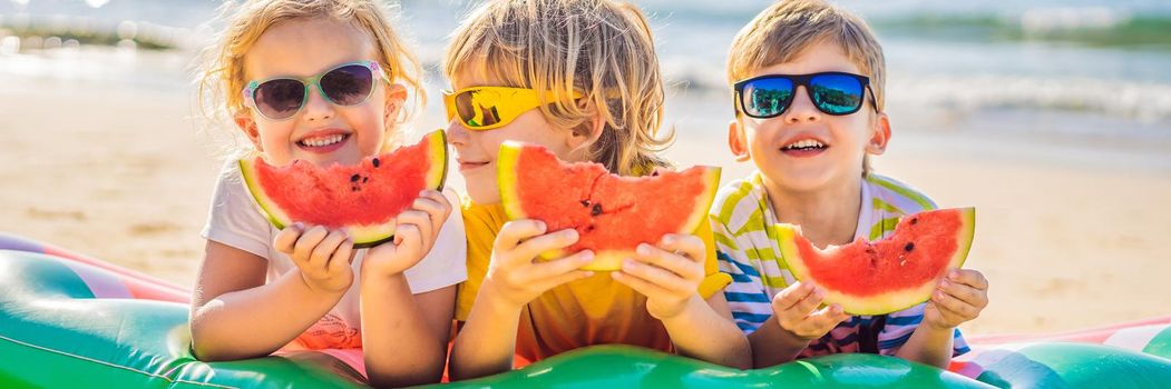 Children eat watermelon on the beach in sunglasses. BANNER, LONG FORMAT