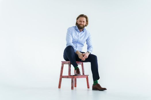 a handsome brutal bearded and long-haired man, a stylish businessman sitting on a chair with a white background. High quality photo