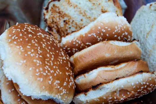 Grilled hamburger buns with sesame seeds in a metal bowl.