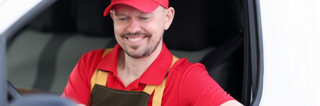 Unshaven male courier sits in the car looking at the delivery address, close-up. Uniformed postman, transportation, address delivery