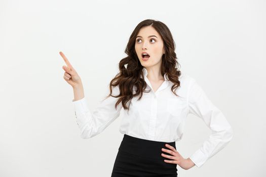 Business Concept: Portrait of surprised young businesswoman pointing finger away to copy space. Isolated on a white background