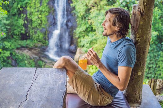 Closeup portrait image of a beautiful man drinking ice tea with feeling happy in green nature and waterfall garden background.