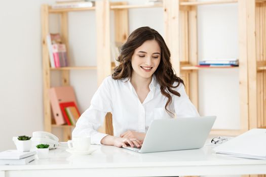 Young businesswoman or secretary sitting at desk and working. Smiling and looking at camera.