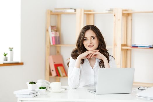 Young businesswoman or secretary sitting at desk and working. Smiling and looking at camera.