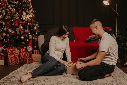 man and woman couple in love open gift boxes untie a bow near the christmas tree. decorated house for New Year. Christmas morning. apartment interior. Valentine's Day celebration