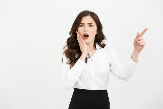 Business Concept: Portrait of surprised young businesswoman pointing finger away to copy space. Isolated on a white background