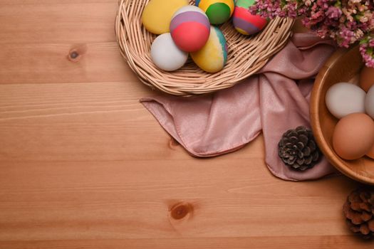 Colorful Easter eggs in wicker basket on wooden background with copy space.