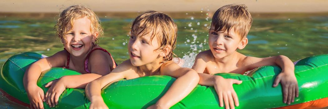 Children swim in the sea on an inflatable mattress and have fun. BANNER, LONG FORMAT