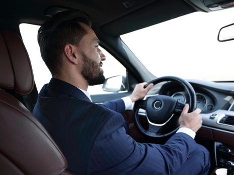 Confident businessman sits at the wheel in his car and looks at the road. Lifestyle