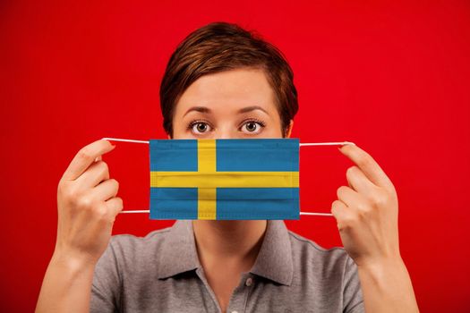 Coronavirus COVID-19 in Sweden. Woman in medical protective mask with the image of the flag of Sweden. The concept of preventing the spread of the epidemic and treating coronavirus.