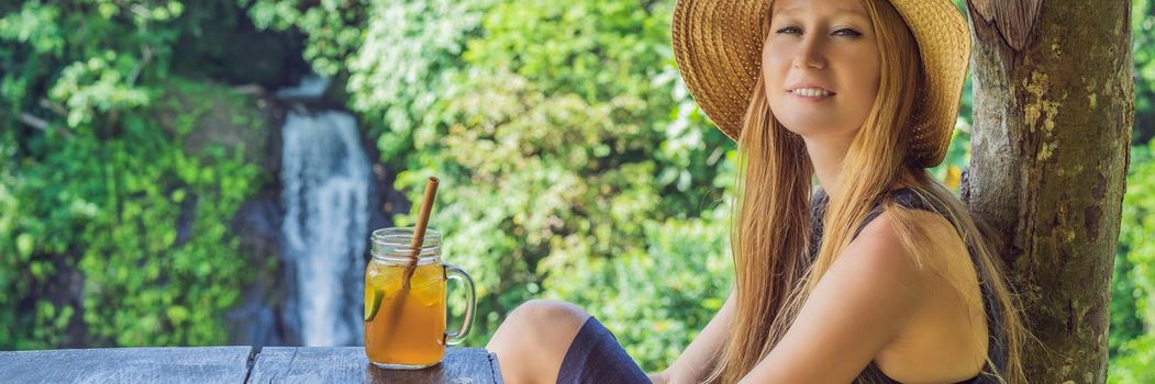 Closeup portrait image of a beautiful woman drinking ice tea with feeling happy in green nature and waterfall garden background. BANNER, LONG FORMAT