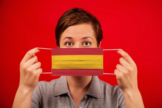 Coronavirus COVID-19 in Spain. Woman in medical protective mask with the image of the flag of Spain. The concept of preventing the spread of the epidemic and treating coronavirus.
