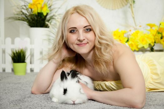 A lovely young blond woman standing in profile closeup and holding a young bunny in her arms. Beautiful blonde girl holding a white rabbit in her arms. Easter bunny sitting in the arms of a girl