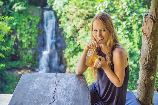 Closeup portrait image of a beautiful woman drinking ice tea with feeling happy in green nature and waterfall garden background.