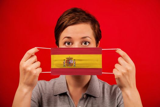Coronavirus COVID-19 in Spain. Woman in medical protective mask with the image of the flag of Spain. The concept of preventing the spread of the epidemic and treating coronavirus.