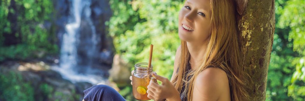 Closeup portrait image of a beautiful woman drinking ice tea with feeling happy in green nature and waterfall garden background. BANNER, LONG FORMAT