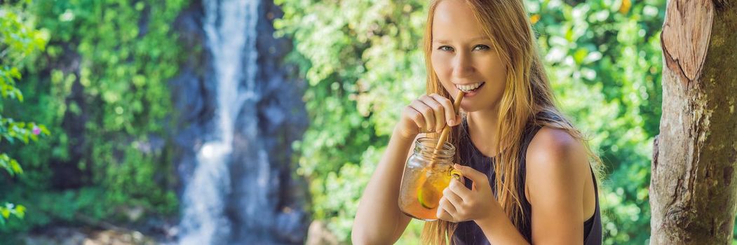 Closeup portrait image of a beautiful woman drinking ice tea with feeling happy in green nature and waterfall garden background. BANNER, LONG FORMAT