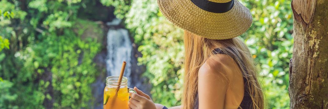 Closeup portrait image of a beautiful woman drinking ice tea with feeling happy in green nature and waterfall garden background. BANNER, LONG FORMAT