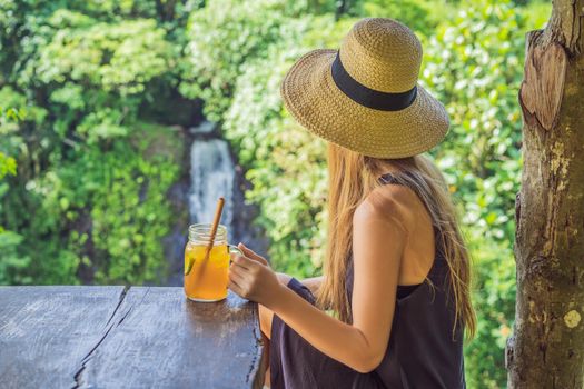 Closeup portrait image of a beautiful woman drinking ice tea with feeling happy in green nature and waterfall garden background.