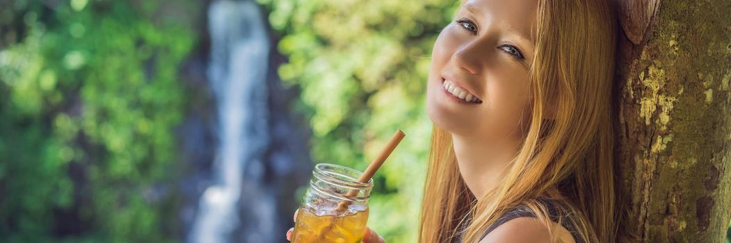 Closeup portrait image of a beautiful woman drinking ice tea with feeling happy in green nature and waterfall garden background. BANNER, LONG FORMAT