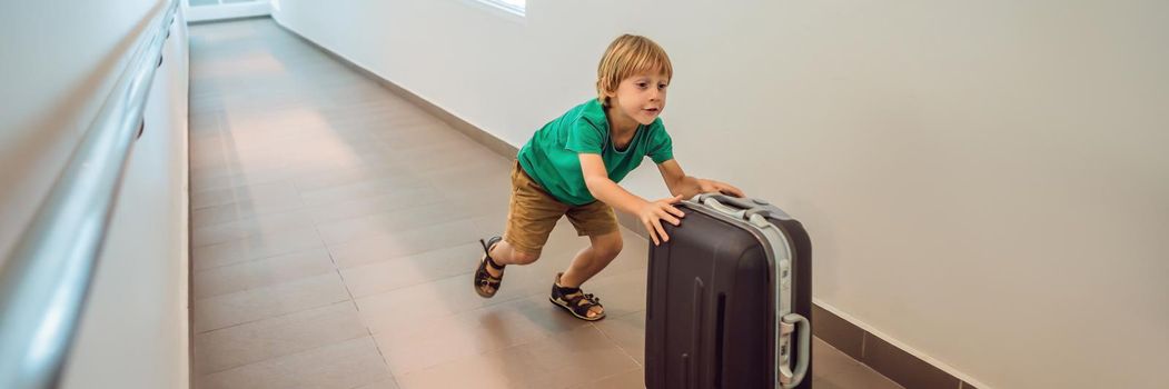 Funny little boy going on vacations trip with suitcase at airport, indoors. BANNER, LONG FORMAT