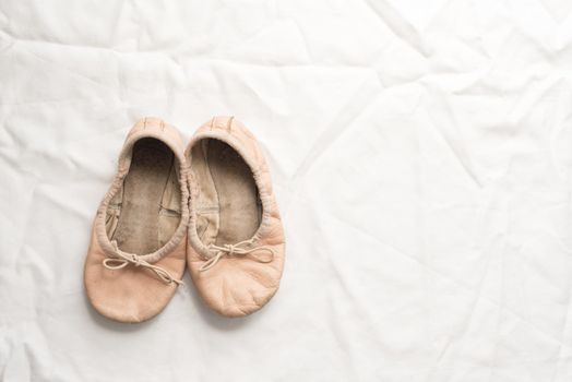 High angle view of old, dirty little girl's pink ballet shoes on crumpled white tablecloth with copy space to right