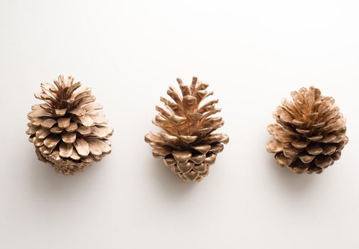 High angle view of three gold painted pine cones on white table