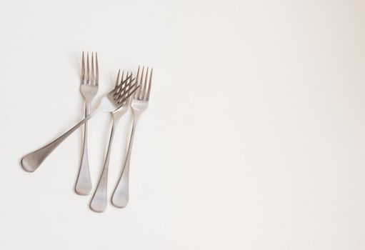 Food background - high angle view of four forks scattered on white table with copy space to right