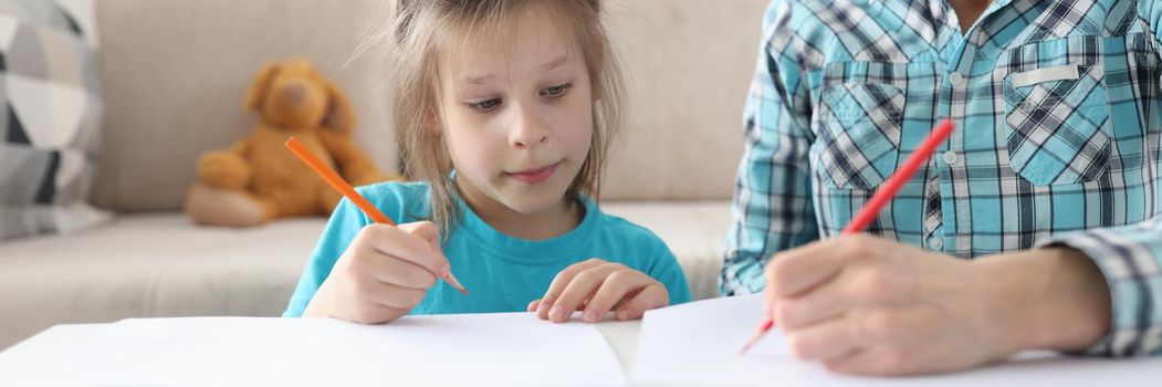 Mom and little daughter are drawing at the table at home, close-up. Preschool education at home. Woman teaches child to draw