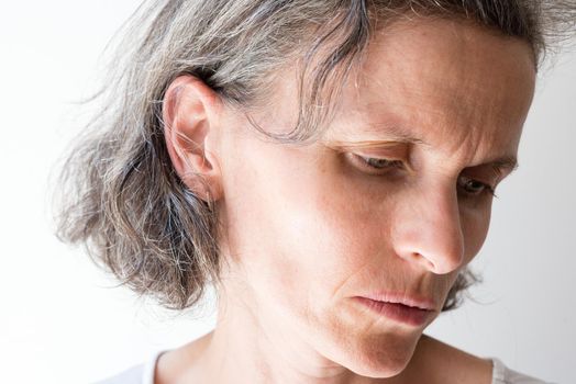 Close up of distressed middle aged woman with grey hair, looking to the side (selective focus)