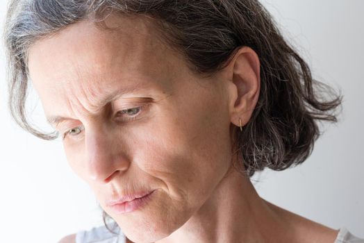 Close up of distressed middle aged woman with grey hair, looking to the side (selective focus)