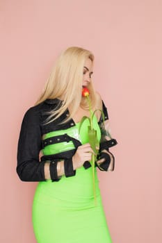 Young elegant woman in trendy jeans jacket. Blonde hair, green dress, isolated over pink background, studio shot. Fashion spring lookbook. Model woman with red tulips in her hands