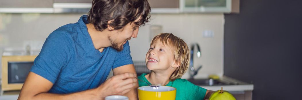 Father and son are talking and smiling while having a breakfast in kitchen. BANNER, LONG FORMAT