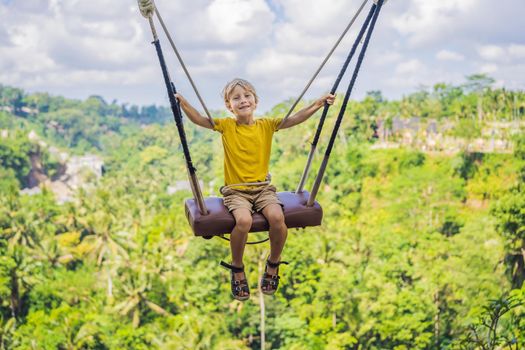 Young boy swinging in the jungle rainforest of Bali island, Indonesia. Swing in the tropics. Swings - trend of Bali. Traveling with kids concept. What to do with children. Child friendly place.