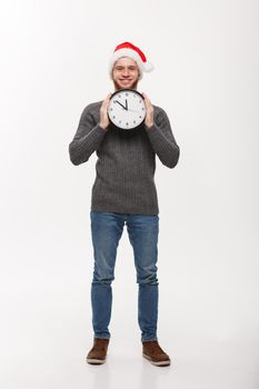 Holiday concept - Young handsome beard man hidden behind white clock over white studio background.