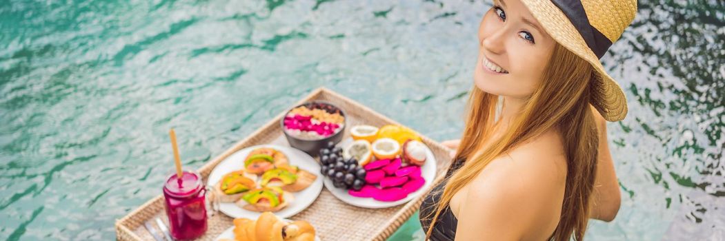 BANNER, LONG FORMAT Breakfast tray in swimming pool, floating breakfast in luxury hotel. Girl relaxing in the pool drinking smoothies and eating fruit plate, smoothie bowl by the hotel pool. Exotic summer diet. Tropical beach lifestyle. Bali Trend.