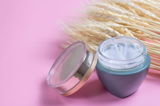 Natural cosmetics made from wheat and barley. Cosmetic jar with cream and wheat ears on a pink background.